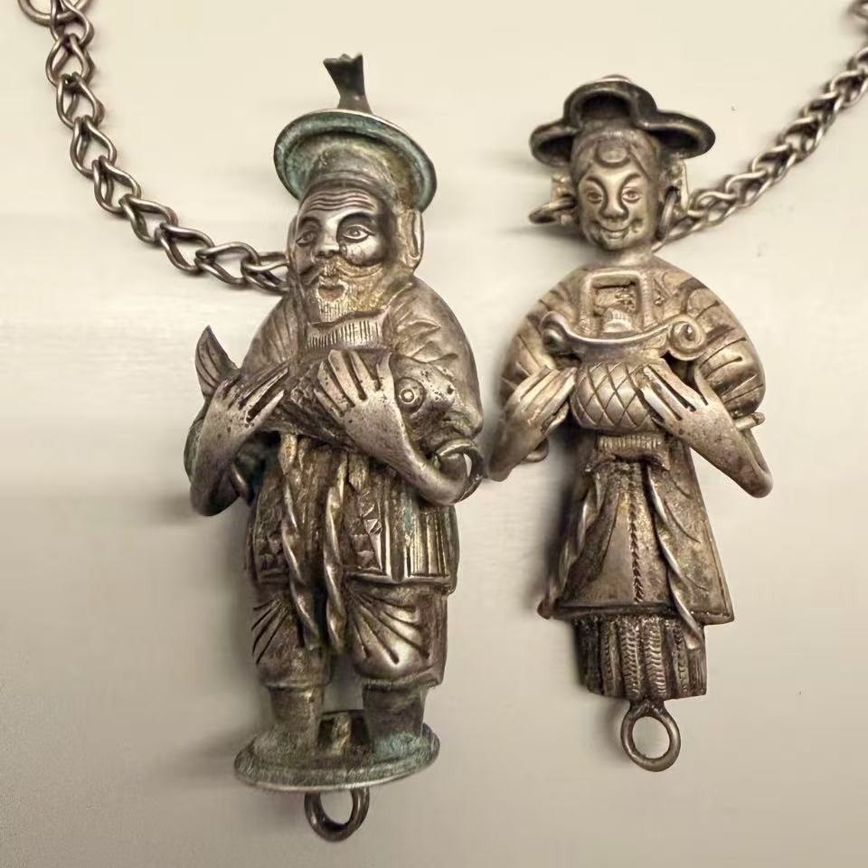 A pair of old Chinese silver figural pendants: a bearded fisherman holding a carp and a lady holding a gold ingot